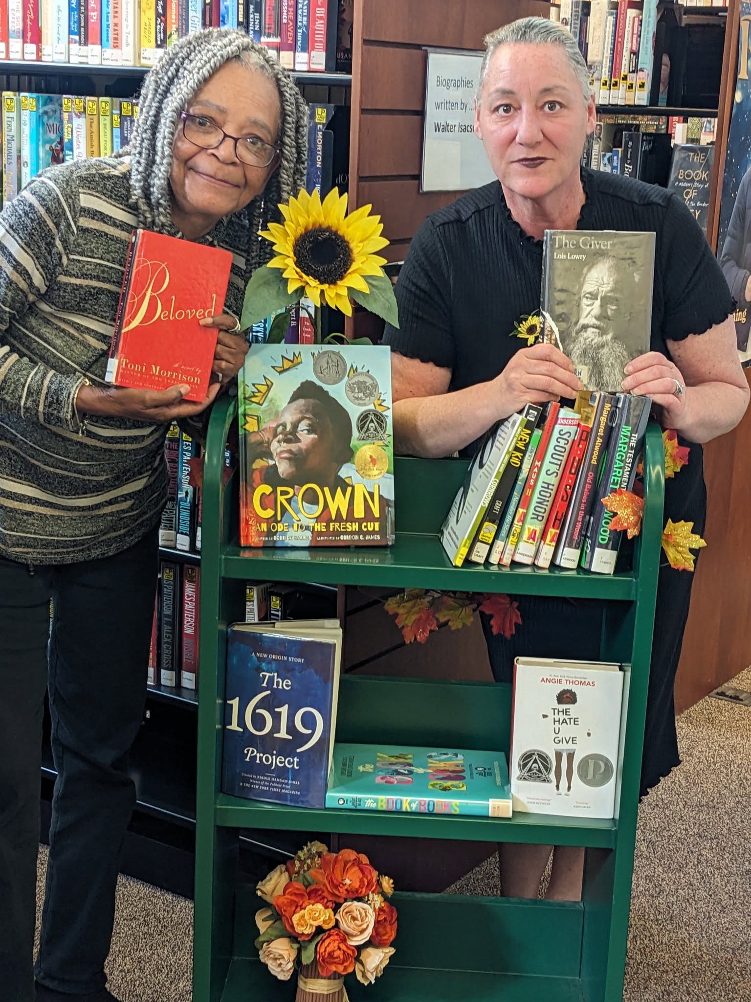 Collette and a patron holding books from a curated library display